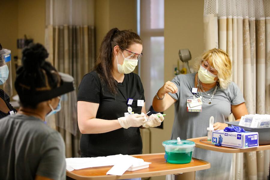 A 大学 of 罗彻斯特 护理学院 student is being taught how to handle medical equipment in a hospital setting.